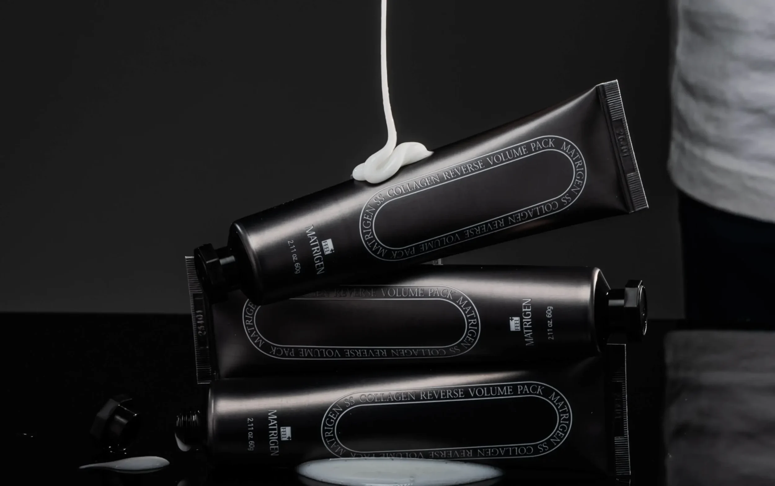 Stapel schwarzer Matrigen-Tuben mit herabtropfender weisser Creme